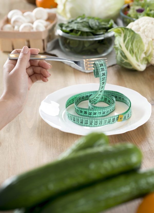 woman-s-hand-holding-fork-with-green-measurement-tape-white-plate-kitchen-counter woman-s-hand-holding-fork-with-green-measurement-tape-white-plate-kitchen-counter