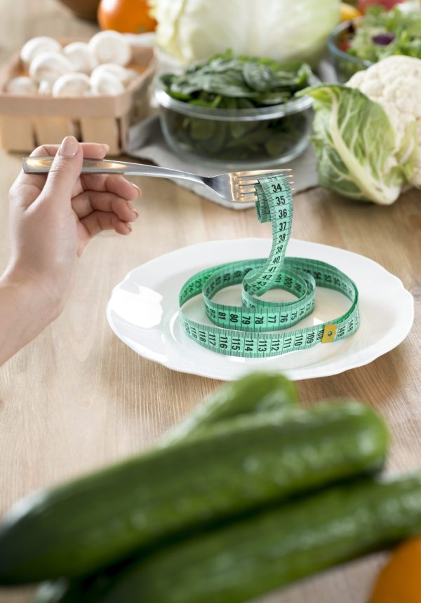 woman-s-hand-holding-fork-with-green-measurement-tape-white-plate-kitchen-counter woman-s-hand-holding-fork-with-green-measurement-tape-white-plate-kitchen-counter